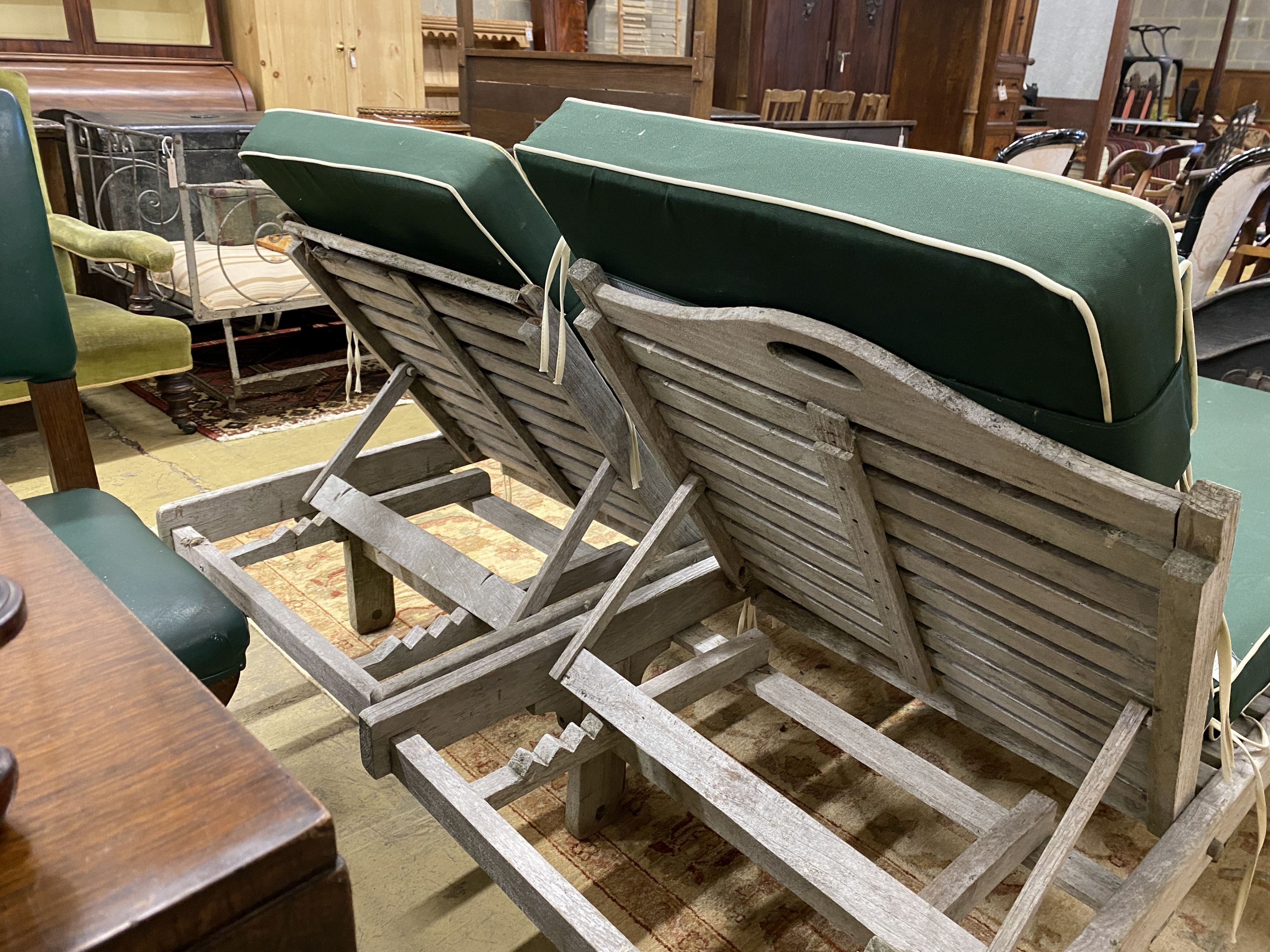 A pair of weathered teak garden loungers with loose cushions, length 200cm, width 67cm